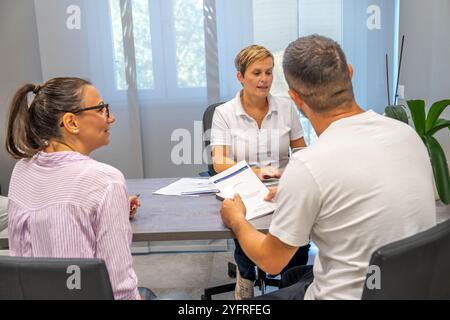 Ärztin berät mit Frau und Ehemann und bietet medizinischen Rat für ein junges Paar im Amt. Stockfoto