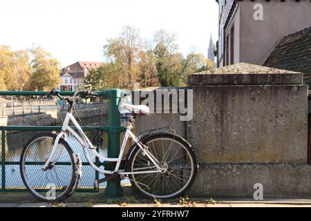 Ein weißes Fahrrad ist an einen Brückenzaun über einem Fluss in Straßburg, Frankreich, 2024 gekettet Stockfoto