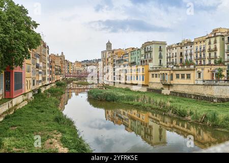 Farbenfrohe gelbe und orangefarbene Häuser und Brücke Pont de Sant Agusti spiegelten sich im Fluss Onyar in Girona, Katalonien, Spanien, wider. Kirche von Sant Feliu und Stockfoto