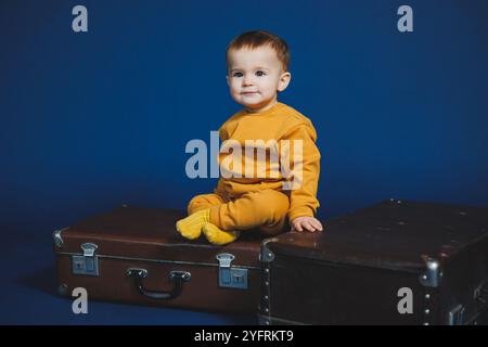 Ein kleiner Junge von 1 Jahr in einem gelben Strickanzug auf blauem Hintergrund. Alltagsgegenstände für Kinder. Stockfoto