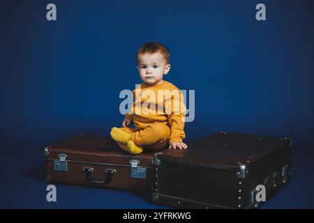 Ein kleiner Junge von 1 Jahr in einem gelben Strickanzug auf blauem Hintergrund. Alltagsgegenstände für Kinder. Stockfoto