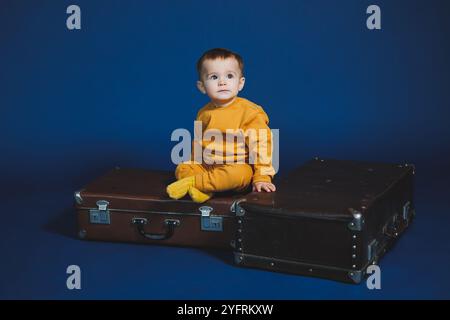 Ein kleiner Junge von 1 Jahr in einem gelben Strickanzug auf blauem Hintergrund. Alltagsgegenstände für Kinder. Stockfoto