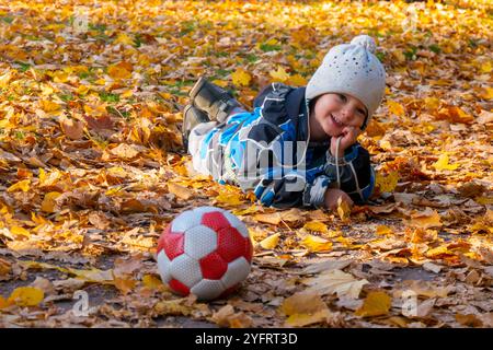 Junge im Herbstpark mit Laub. Er liegt auf den gelben Blättern. Stockfoto