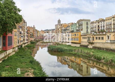 Farbenfrohe gelbe und orangefarbene Häuser und Brücke Pont de Sant Agusti spiegelten sich im Fluss Onyar in Girona, Katalonien, Spanien, wider. Kirche von Sant Feliu und Stockfoto