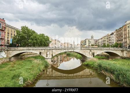 Farbenfrohe gelbe und orangefarbene Häuser und Brücke Pont de Sant Agusti spiegelten sich im Fluss Onyar in Girona, Katalonien, Spanien, wider. Kirche von Sant Feliu und Stockfoto