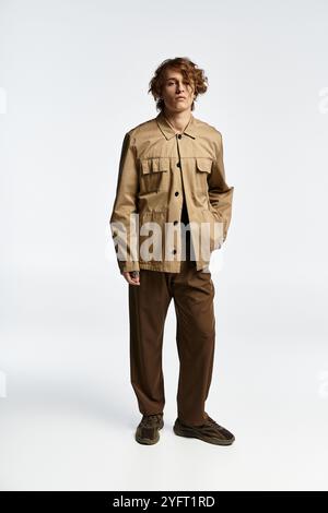 Ein hübscher junger Mann mit welligen Haaren zeigt einen trendigen Herbstlook in einem eleganten Studio-Setting. Stockfoto