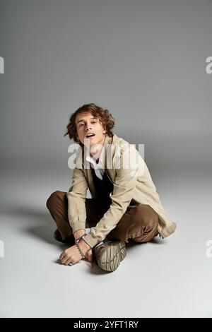 Ein hübscher junger Mann mit welligen Haaren zeigt ein trendiges Herbstoutfit, während er anmutig sitzt. Stockfoto