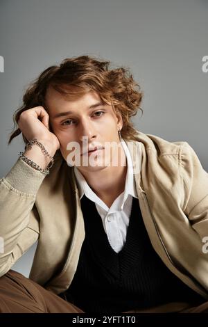 Ein hübscher junger Mann mit welligen Haaren zeigt einen eleganten Herbstlook und zeigt eine besinnliche Pose. Stockfoto