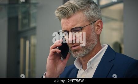 Ernsthafter erwachsener Unternehmer mittlerer Alter Geschäftsmann in der Stadt in der Nähe von Geschäftsgebäuden verwirrte Antwort Anruf aufgebracht besorgt Brille abzunehmen Senior Stockfoto