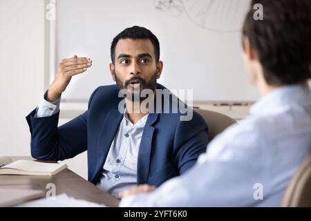 Inspirierte indische Geschäftsleute, die mit männlichen Kollegen im Büro sprechen Stockfoto