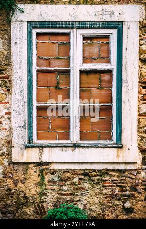 Das verwitterte Fenster verfügt über Holzläden mit teilweise offenen Lamellen, die von einer zerbröckelnden Steinmauer eingerahmt werden Stockfoto