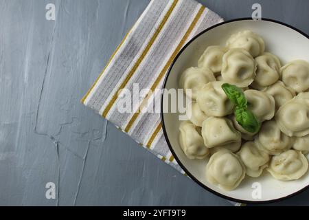 Gefüllte Knödel auf einem Teller auf einer Serviette mit Kräutern, Basilikum auf grauem Hintergrund mit einem Kopierraum la Text. Draufsicht von oben. Stockfoto