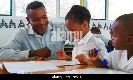 Ein Lehrer arbeitet mit zwei Schülern zusammen, die an ihren Aufgaben arbeiten. Stockfoto