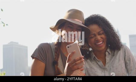 Zwei Freundinnen, Die Fotos Auf Dem Telefon Anschauen Und Lachen Von Manhattan Skyline Stockfoto