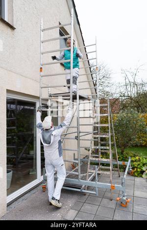 Gerüstbauerin, Malerin und Maler bauen ein mobiles Gerüst am Einfamilienhaus auf, Modell freigegeben für redaktionelle Nutzung, Gerüstbauer *** Gerüstbauer, Maler und Maler, die ein mobiles Gerüst auf einem Einfamilienhaus aufstellen, Modell freigegeben für redaktionelle Nutzung, Gerüstbauer 20241105-DSC 8690 Stockfoto