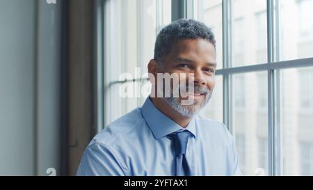 Kopf Und Schultern Porträt Eines Lächelnden Reifen Geschäftsmannes, Der Im Büro Am Fenster Steht Stockfoto