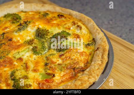 Ein Nahaufnahme einer hausgemachten Quiche mit goldener Kruste, gefüllt mit Brokkoli-Röschen und einer käsigen, cremigen Füllung, perfekt gebacken auf einem Holzschnitt bo Stockfoto