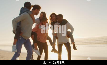 Gruppe Junger Freunde, Die Zusammen Mit Lens Flare Am Winter Beach Ein Huckepack-Rennen Machen Stockfoto