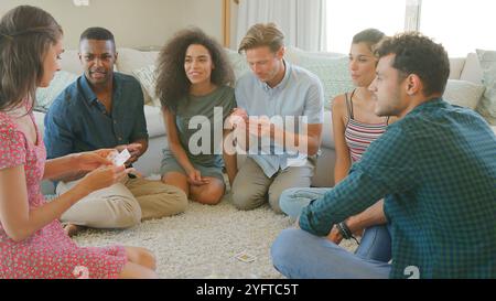 Gruppe Junger Freunde, Die Zu Hause Auf Dem Boden Sitzen Und Gemeinsam Karten Spielen Stockfoto