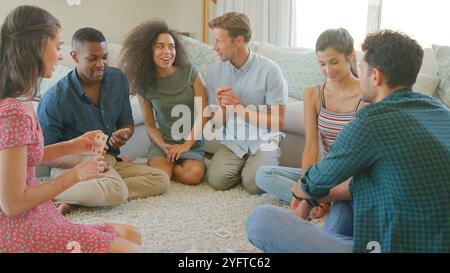Gruppe Junger Freunde, Die Zu Hause Auf Dem Boden Sitzen Und Gemeinsam Karten Spielen Stockfoto