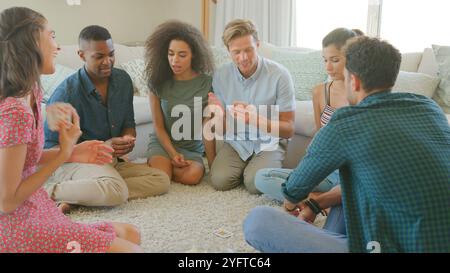 Gruppe Junger Freunde, Die Zu Hause Auf Dem Boden Sitzen Und Gemeinsam Karten Spielen Stockfoto