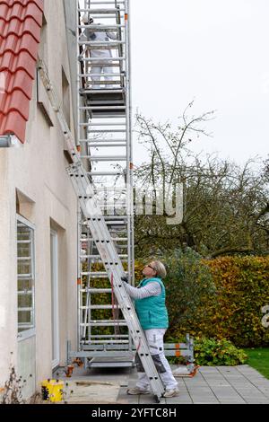 Malerin baut die Schiebeleiter am Giebel eines Hauses auf. Vorarbeiten zum Malern des Dachüberstands, Modell freigegeben für redaktionelle Nutzung, Dachüberstand streichen *** Maler stellt die Schiebeleiter auf den Giebelgiebel eines Hauses auf Vorarbeiten zur Bemalung des Dachüberhangs, Modell freigegeben für redaktionelle Nutzung, Bemalen des Dachüberhangs 20241105-DSC 8776 Stockfoto