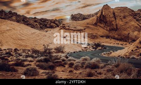 Die Blacktop Road schlängelt sich in der Dämmerung durch den Red Rocks Canyon. Die Sonne in der Ferne geht auf den glatten Felswänden unter. Stockfoto