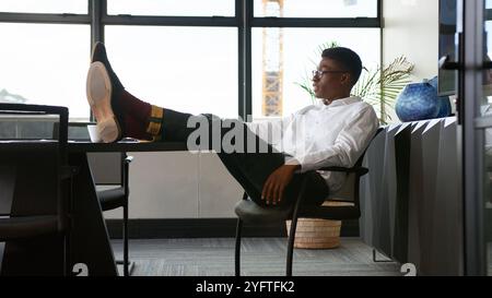 Junger Geschäftsmann, Der Im Büro Sitzt Und Die Füße Auf Seinem Schreibtisch Im Büro Sitzt Stockfoto