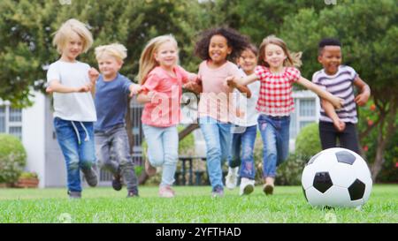 Gruppe Von Kindern, Die Mit Freunden Im Park Fußball Spielen, Läuft In Richtung Ball Im Vordergrund Stockfoto