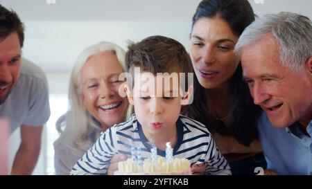 Die Familie Der Mehrgenerationen Feiert Den Geburtstag Mit Dem Enkel Zu Hause, Während Er Kerzen Ausbläst Stockfoto