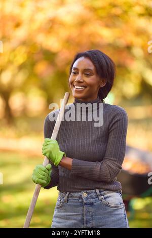 Eine Junge Frau Mit Barrow, Die Im Herbstgarten Blätter Harkt Stockfoto