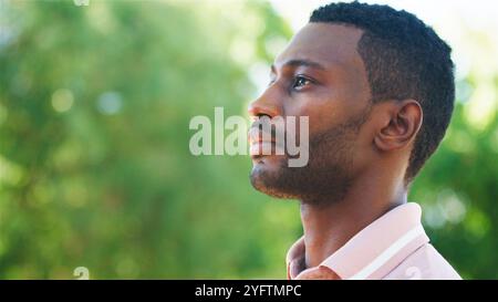 Eine Person steht ruhig und blickt nachdenklich in die Ferne, während sie von lebhaftem Grün umgeben ist. Die Sonne scheint warm und hebt die Ruhe hervor Stockfoto