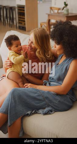 Zwei Frauen spielen fröhlich mit einem entzückenden Baby, während sie auf einer bequemen Couch in einem hellen, einladenden Wohnzimmer sitzen. Ihre Ausdrücke strahlen aus Stockfoto