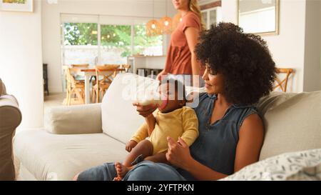 Die Frau ernährt liebevoll das Kind, während ein anderer Erwachsener im Hintergrund ist. Stockfoto