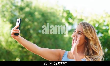 Frau, die einen sonnigen Tag genießt, während sie ein Selfie im Park macht. Stockfoto