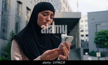 Traurige Verärgerung betont frustrierte muslimische Geschäftsfrau islamische Geschäftsfrau Mädchen weiblich in schwarzem Hijab Arbeitgeberversagen verlor Problem schlechte Nachrichten Handy Stockfoto