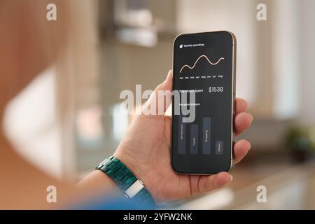 Eine Person analysiert ihre monatlichen Ausgaben mithilfe einer Smartphone-Anwendung. Das Gerät zeigt finanzielle Einblicke und Ausgabentrends auf dem Bildschirm an. Stockfoto