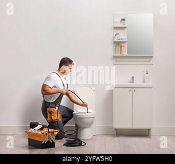 Klempner benutzen eine Ablaufschlange für verstopfte Toilette im Badezimmer Stockfoto