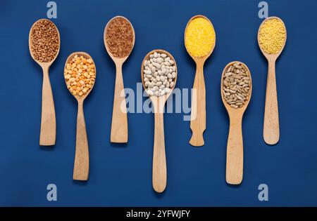 Verschiedene Getreidesorten, Samen und Hülsenfrüchte in Löffeln auf blauem Holztisch, flach gelegt Stockfoto