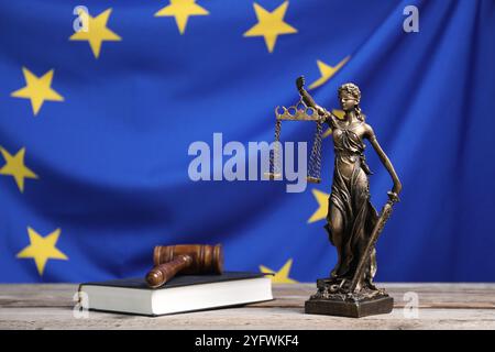 Figur der Justizfrau, richterlicher Hammer und Buch auf Holztisch vor der Flagge der Europäischen Union Stockfoto