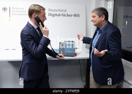 Freital, Deutschland. November 2024. Michael Kretschmer (CDU), Ministerpräsident von Sachsen, hält neben der BSI-Präsidentin Claudia Plattner ein Telefon für die Hochsicherheits-Telefonielösung zur Kommunikation von Verschlusssachen beim Bundesamt für Sicherheit in der Informationstechnik (BSI). Die Telefonielösung wird in Sachsen getestet. Quelle: Sebastian Kahnert/dpa/Alamy Live News Stockfoto