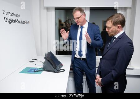 Freital, Deutschland. November 2024. Günther Welsch (l), Leiter der Abteilung Kryptotechnologie, erklärt dem sächsischen Ministerpräsidenten Michael Kretschmer (CDU) ein Telefon für die Hochsicherheits-Telefonielösung zur Übermittlung von Verschlusssachen beim Bundesamt für Sicherheit in der Informationstechnik (BSI). Die Telefonielösung ist für den Testbetrieb in Sachsen vorgesehen. Quelle: Sebastian Kahnert/dpa/Alamy Live News Stockfoto