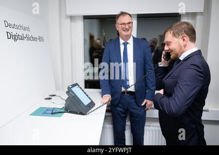 Freital, Deutschland. November 2024. Günther Welsch (l), Leiter der Abteilung Kryptotechnologie, erklärt dem sächsischen Ministerpräsidenten Michael Kretschmer (CDU) ein Telefon für die Hochsicherheits-Telefonielösung zur Übermittlung von Verschlusssachen beim Bundesamt für Sicherheit in der Informationstechnik (BSI). Die Telefonielösung ist für den Testbetrieb in Sachsen vorgesehen. Quelle: Sebastian Kahnert/dpa/Alamy Live News Stockfoto