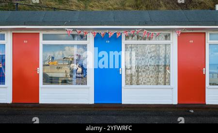 Strandchalets mit weißen und blauen Türen. Farbenfrohe Chalets am Meer in Cromer, Norfolk, einem beliebten englischen Ferienort. Reflexionen in Fenstern. Stockfoto