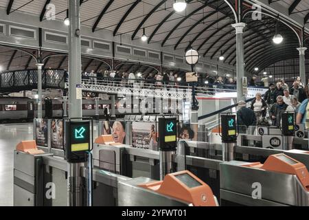 Ticketbarrieren am Bahnhof Newcastle. Ein Zug wartet am Bahnsteig und die Passagiere überqueren die Brücke. Einer der ältesten Bahnhöfe Großbritanniens. Stockfoto