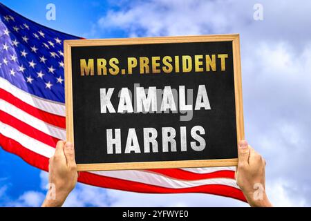 5. November 2024: Siegerin der US-Präsidentschaftswahl: Frau Kamala Harris. Eine Hand hält eine Tafel in der Luft vor der US-Flagge. FOTOMONTAGE *** Wahlsieger der US-Wahl zum Präsidenten der Vereinigten Staaten von Amerika: Frau Präsidentin Kamala Harris. Eine Hand hält eine Tafel in die Luft vor der Flagge der USA. FOTOMONTAGE Stockfoto