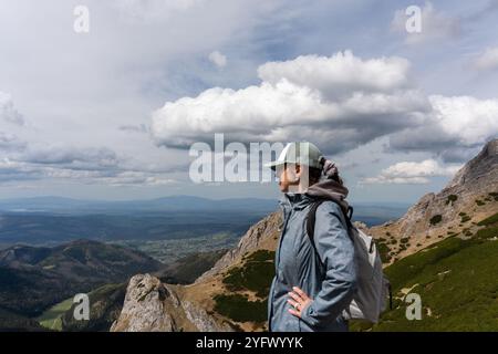 Selbstbewusste Wanderer mit Blick über das malerische Bergtal mit Händen auf den Hüften an bewölkten Tagen im Frühling. Konzept der Erkundung, Outdoor-Abenteuer Stockfoto