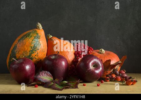Herbststillleben von Kürbis, Äpfeln, Äpfeln, Kastanien und Herbstblättern auf dunklem Holzhintergrund. Herbsternte Stockfoto