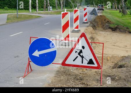 Ein Straßenreparaturbereich, der durch Warn- und Richtungsschilder sowie rot-weiß gestreifte Pfosten und Warnschilder abgegrenzt ist Stockfoto