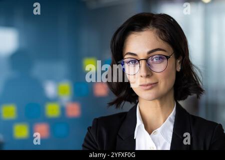 Selbstbewusste junge Geschäftsfrau in Brille und Blazer strahlt Professionalität im Büro aus. Ideale Darstellung von Führung, Unternehmenserfolg und Empowerment. Stockfoto hebt modernes Geschäft hervor. Stockfoto